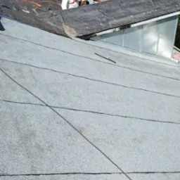 Praca na dachu: dekarz z palnikiem podczas krycia dachu papą termozgrzewalną. Widok z góry na płaski dach z papy i cień fotografa.