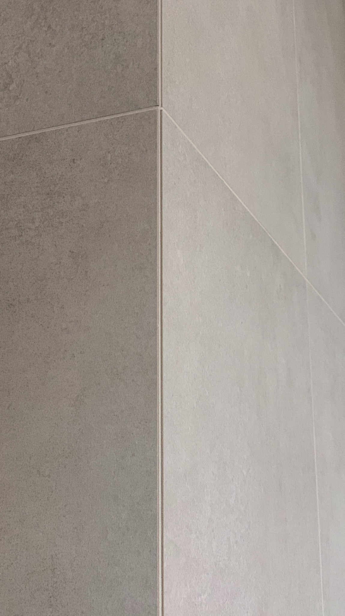 Fragment ściany wyłożonej płytkami w dwóch odcieniach szarości, z widocznymi fugami i krawędziami płytek, ukazujący detale wykończenia.