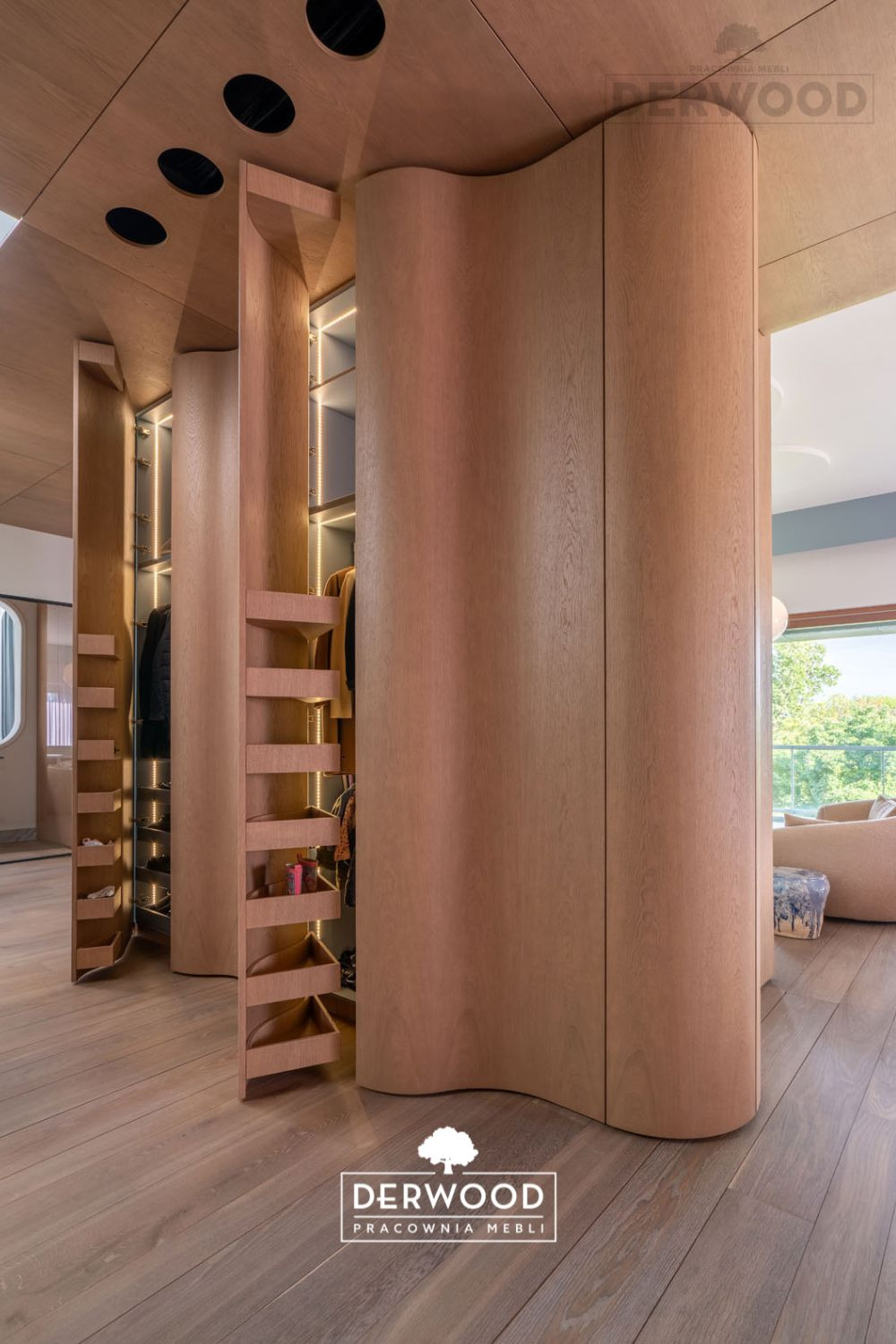 Nowoczesna garderoba z drewna o zaokrąglonych kształtach, z wysuwanymi półkami i oświetleniem LED, widoczna z perspektywy podłogi w jasnym wnętrzu.
