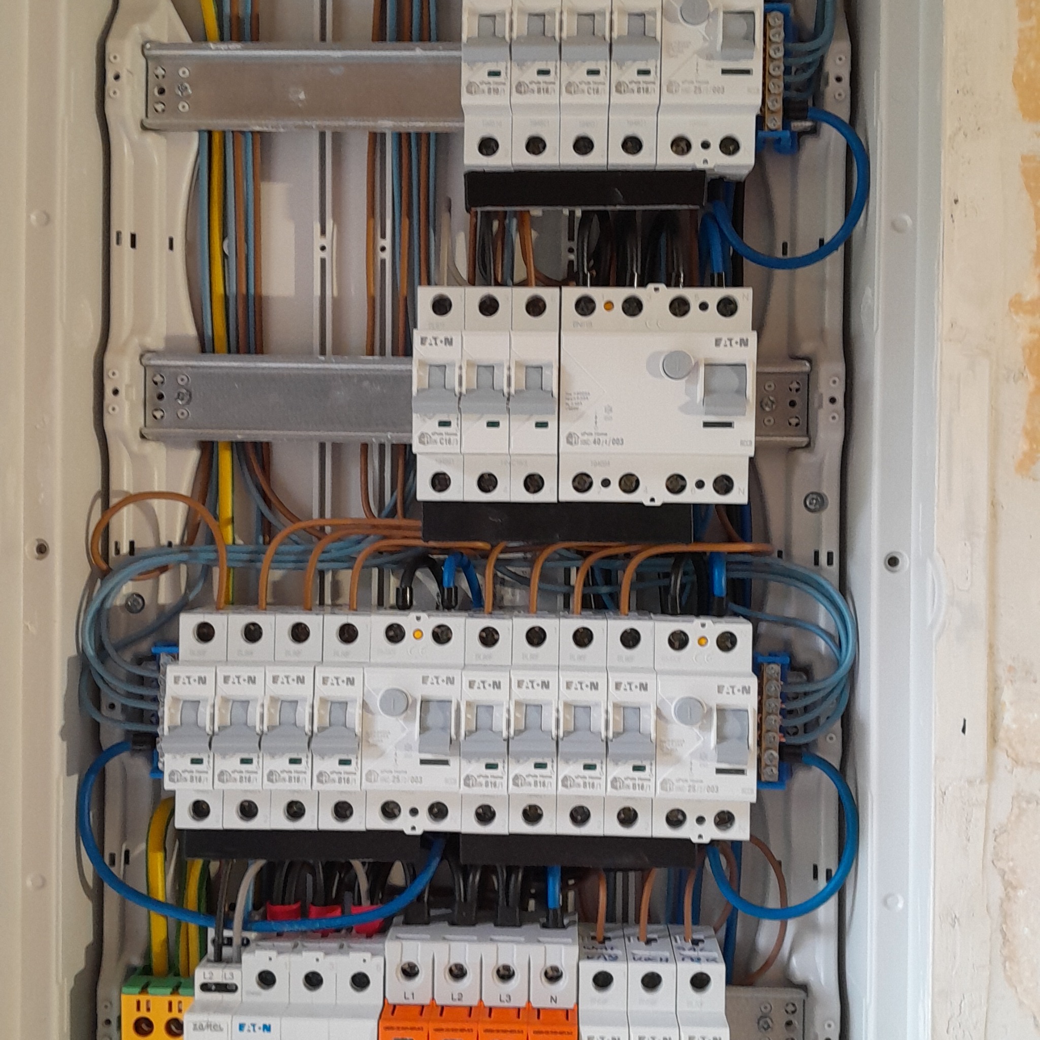 Rozdzielnica elektryczna marki Eaton z zainstalowanymi bezpiecznikami i okablowaniem w kolorach żółtym, niebieskim, brązowym i czarnym, zamontowana w białej obudowie.