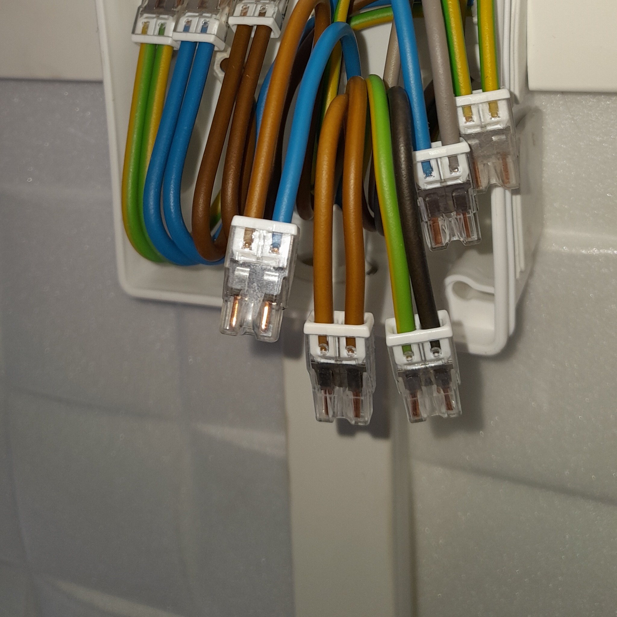 Połączenia elektryczne w puszce instalacyjnej z użyciem szybkozłączek Wago. Widoczne przewody w izolacji: niebieskiej, brązowej, zielono-żółtej i szarej.