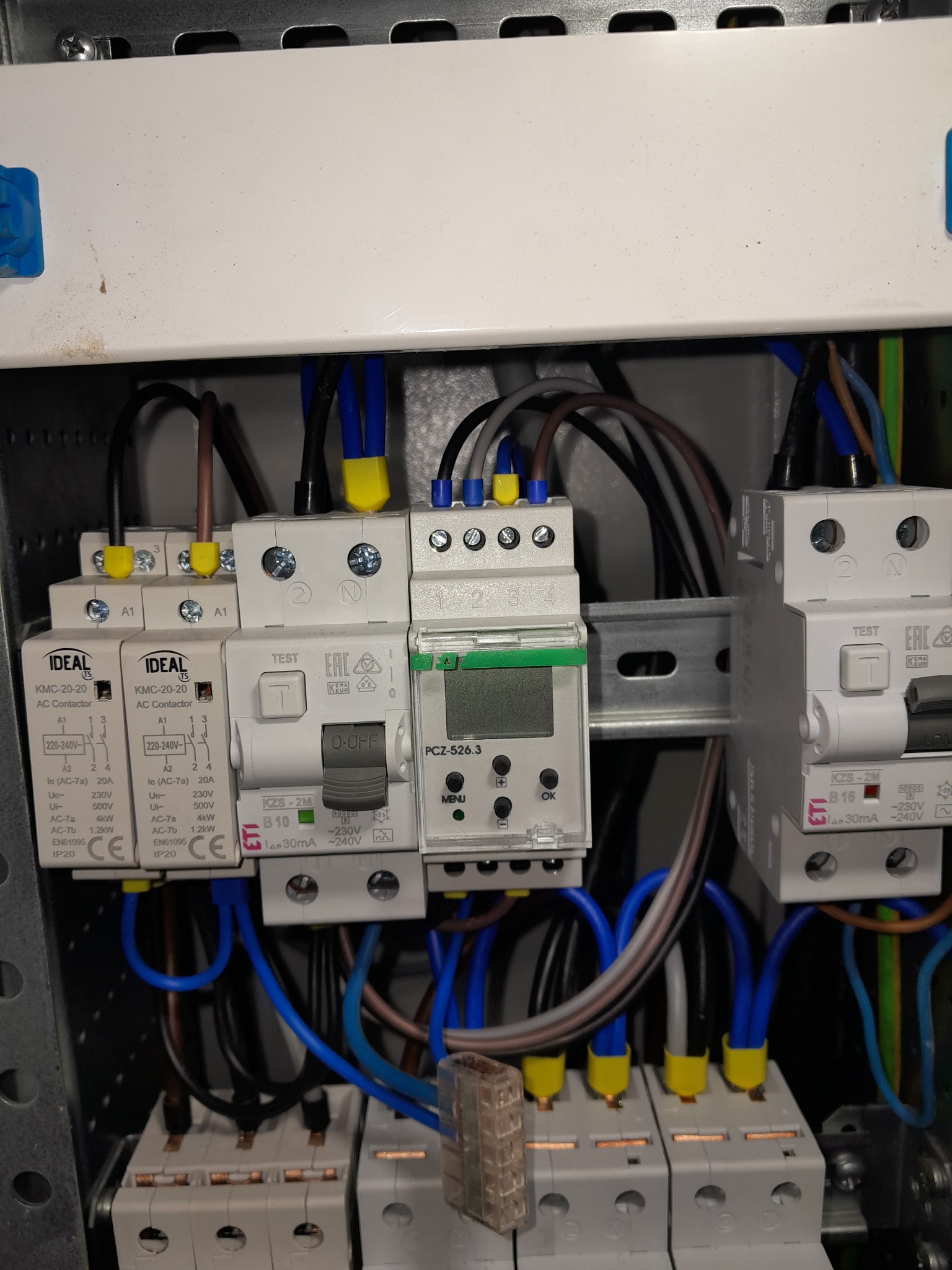 Szafa elektryczna z zainstalowanymi stycznikami, wyłącznikami różnicowoprądowymi i programatorem czasowym. Widoczne przewody w kolorach niebieskim, brązowym i czarnym.