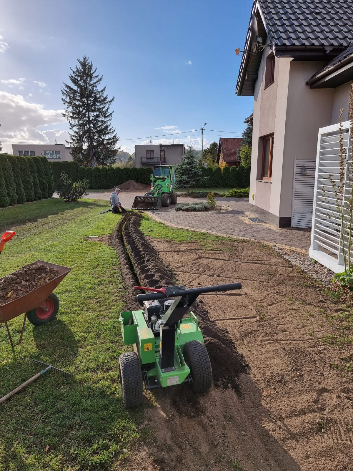 Wykop pod instalacje w ogrodzie przydomowym wykonywany przy użyciu minikoparki i glebogryzarki, widoczny pracownik i taczka z ziemią.