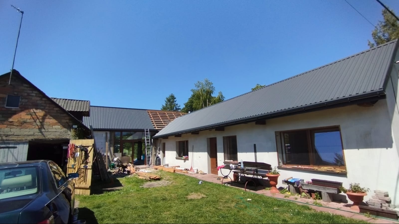 Budynek z częściowo wymienionym pokryciem dachowym z blachy trapezowej w kolorze grafitowym. Widoczne elementy konstrukcji dachu i drabina oparta o budynek.