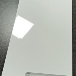 GARDEN SERWIS SPÓŁKA Z OGRANICZONĄ ODPOWIEDZIALNOŚCIĄ - Biały, lakierowany front meblowy z frezowanym uchwytem, leżący na ciemnoszarym blacie z widoczną naklejką 'Komfort Frez Częściowy 2'.