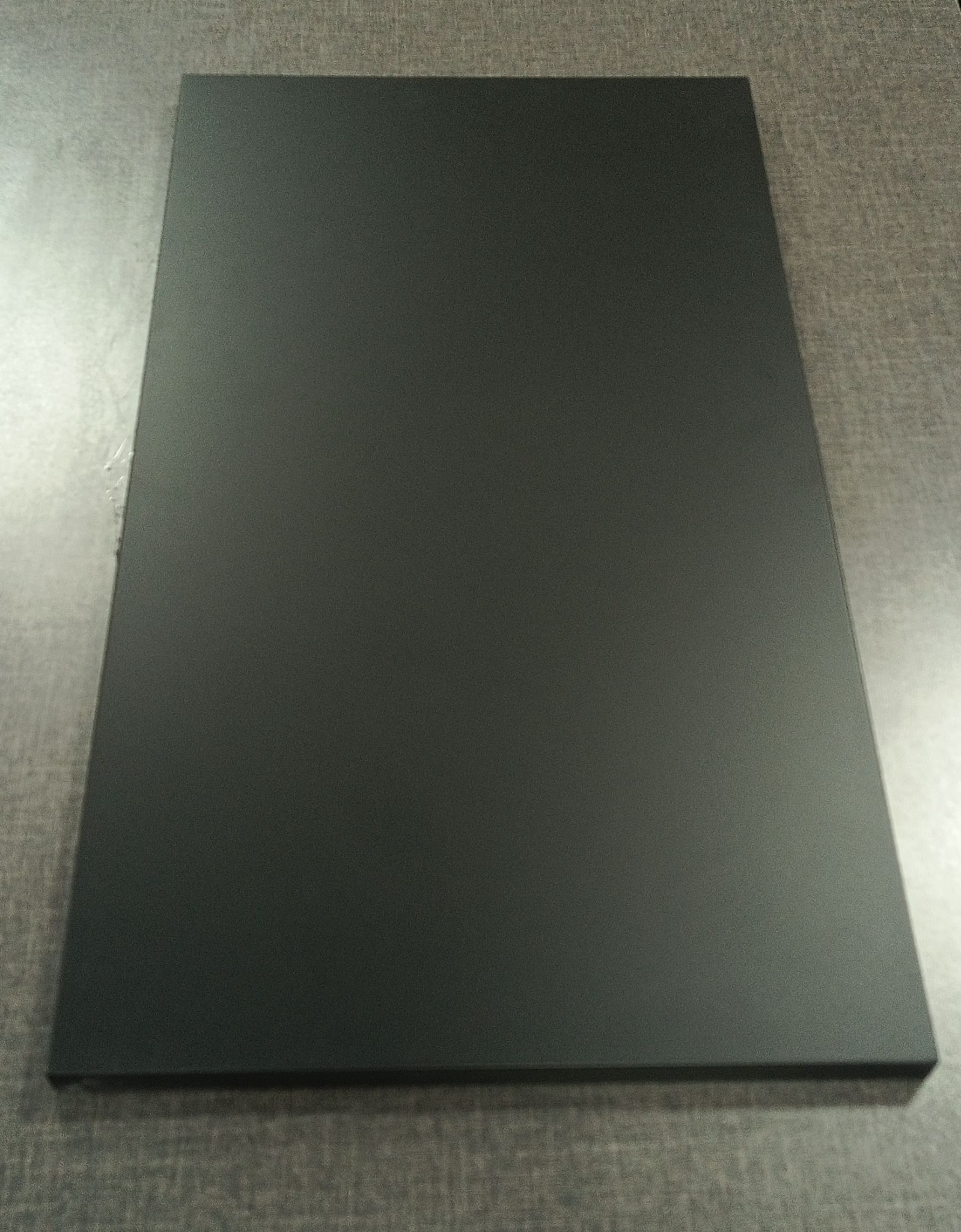 Ciemnoszary, matowy blat z drewna na szarej powierzchni z widoczną fakturą. Kąt ujęcia z góry, oświetlenie studyjne.