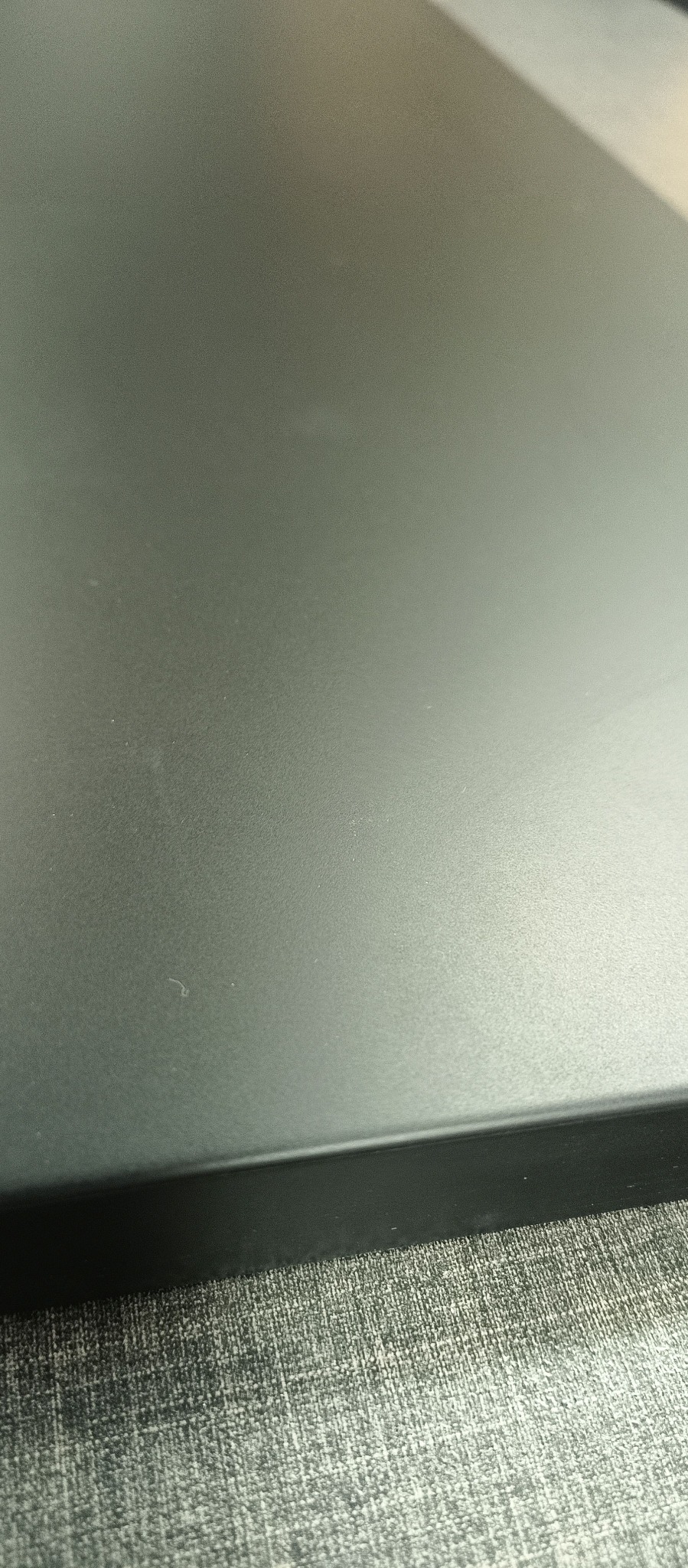 Fragment czarnego blatu z widoczną krawędzią i delikatną fakturą, leżącego na szarej, tekstylnej powierzchni.