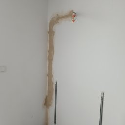 Optiklima - Przygotowanie pod montaż klimatyzacji: wyfrezowana bruzda w ścianie, widoczne uchwyty montażowe i wystające kable. Ściany w kolorze białym, surowy stan wykończenia.