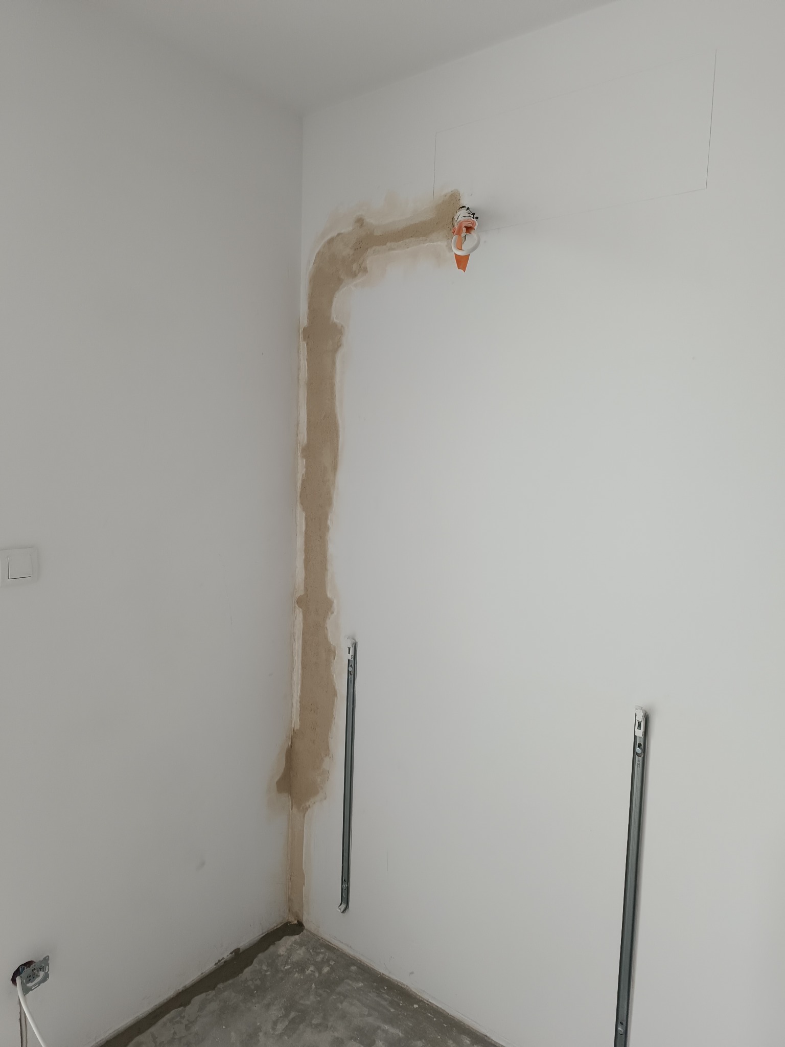 Przygotowanie pod montaż klimatyzacji: wyfrezowana bruzda w ścianie, widoczne uchwyty montażowe i wystające kable. Ściany w kolorze białym, surowy stan wykończenia.