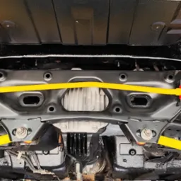 Podwozie samochodu po konserwacji antykorozyjnej, z elementami zawieszenia w jaskrawym żółtym kolorze i nowymi czerwonymi tulejami, widoczne od spodu.