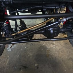 AGAW Patryk Michalak - Podwozie terenowego auta po konserwacji: czarne elementy zawieszenia, złoty drążek stabilizatora, widoczne sprężyny i opony z agresywnym bieżnikiem.