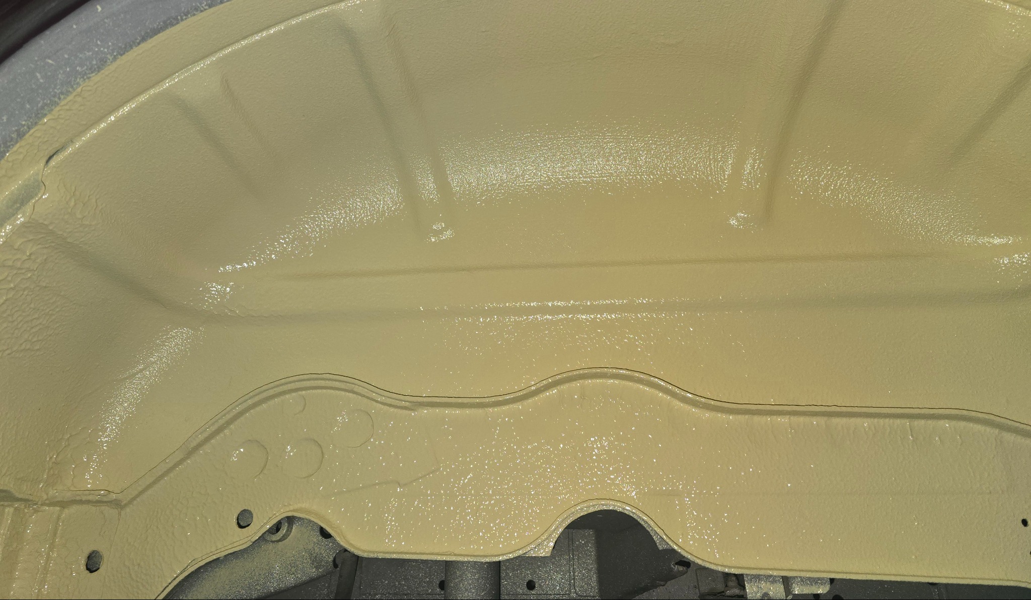 Podwozie samochodu po nałożeniu świeżej, jasnobeżowej warstwy ochronnej. Widoczna struktura powłoki antykorozyjnej z delikatnym połyskiem.