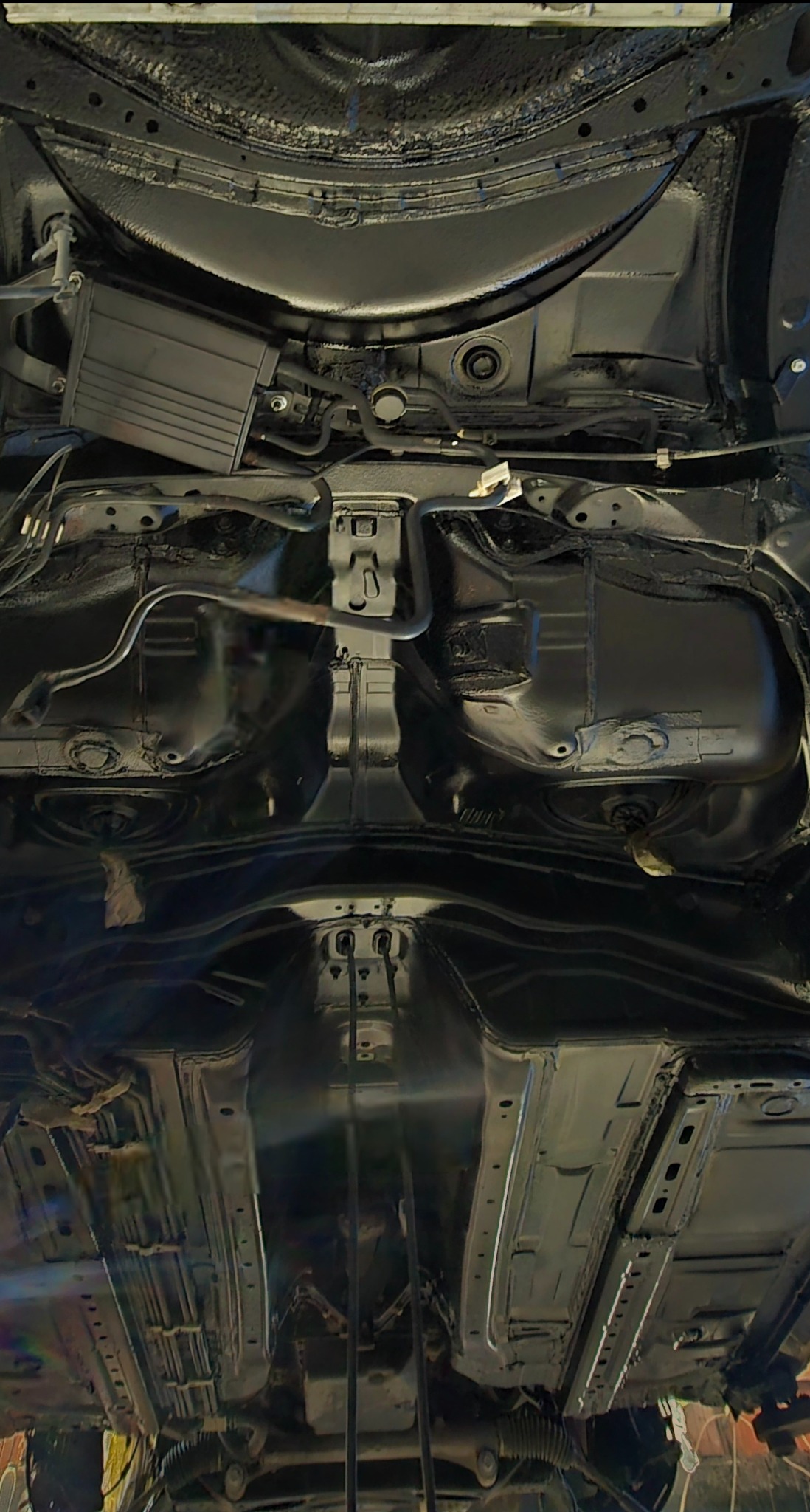 Podwozie samochodu po zabezpieczeniu antykorozyjnym, pokryte czarną, błyszczącą powłoką ochronną, widoczne elementy zawieszenia i układu wydechowego.