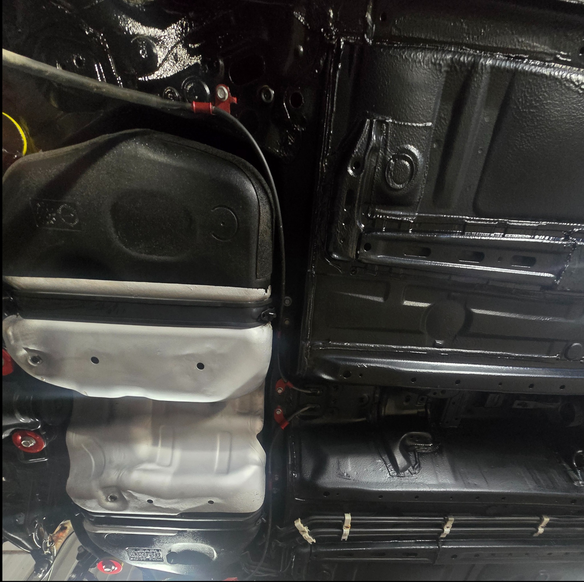 Podwozie samochodu po konserwacji antykorozyjnej, z elementami w kolorze czarnym i srebrnym, widoczne mocowania i przewody.