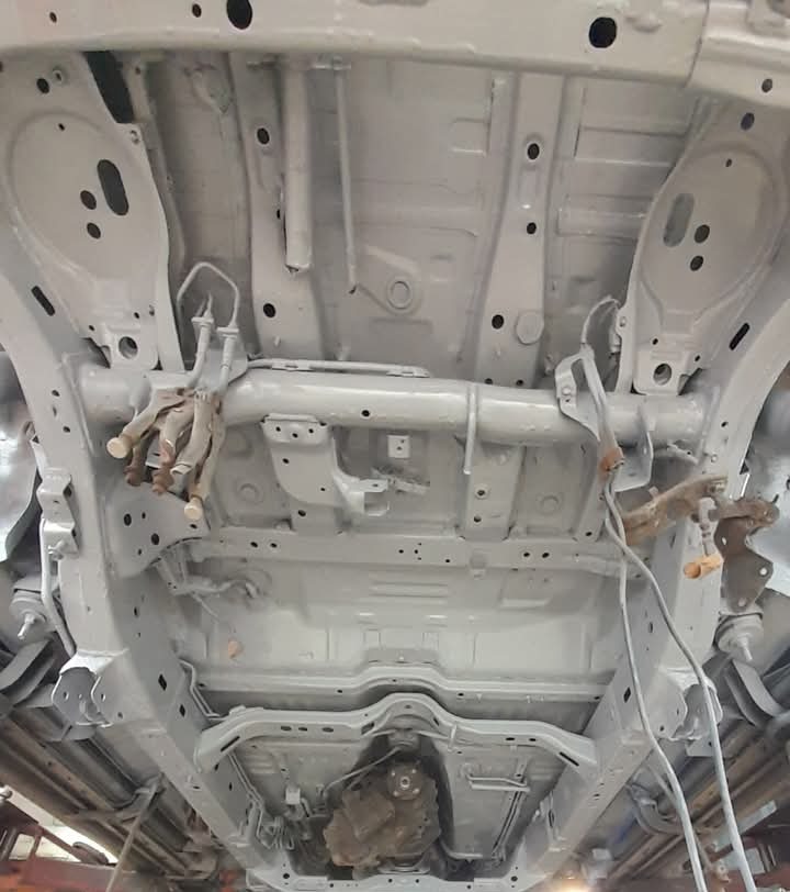 Podwozie samochodu po zabezpieczeniu antykorozyjnym, widok od spodu, szare elementy zawieszenia i karoserii.