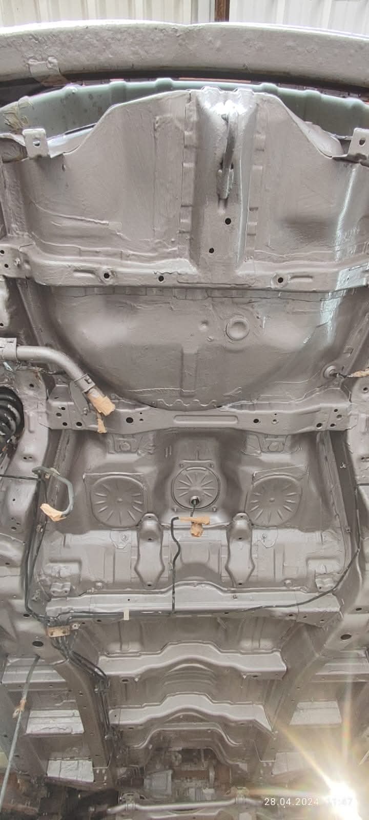 Podwozie samochodu po nałożeniu warstwy ochronnej antykorozyjnej, widoczne elementy zawieszenia i podłogi zabezpieczone taśmą malarską.