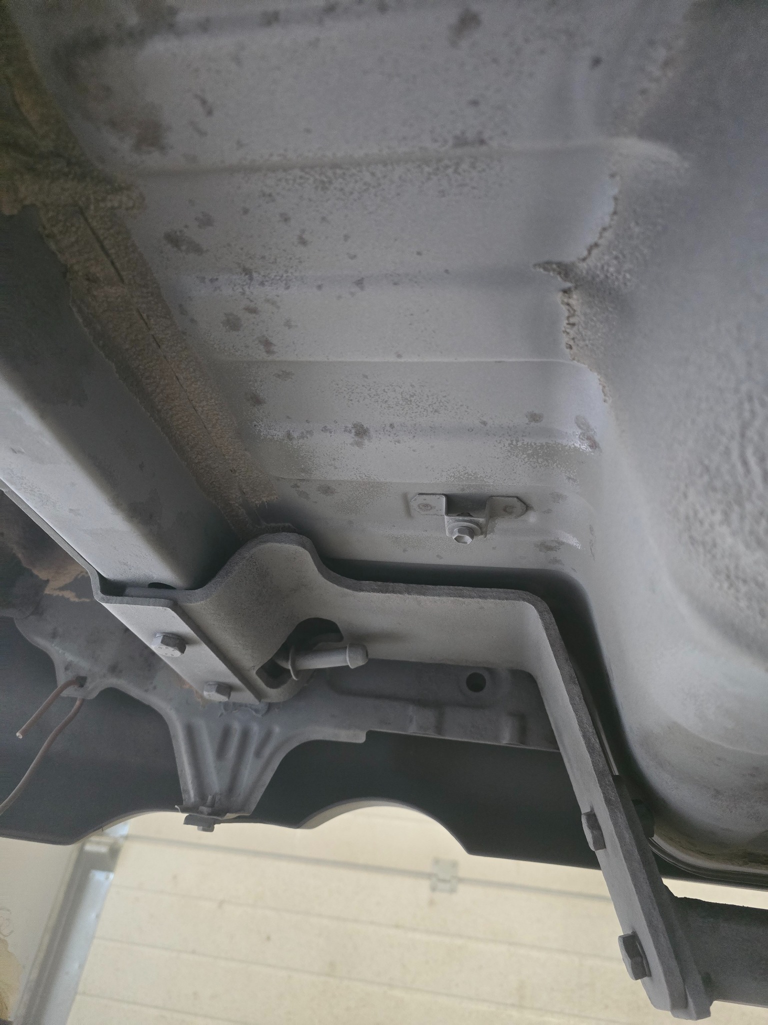 Spód pojazdu z widoczną metalową konstrukcją mocowaną śrubami, prawdopodobnie element podwozia lub mocowanie. Widoczny nalot rdzy.