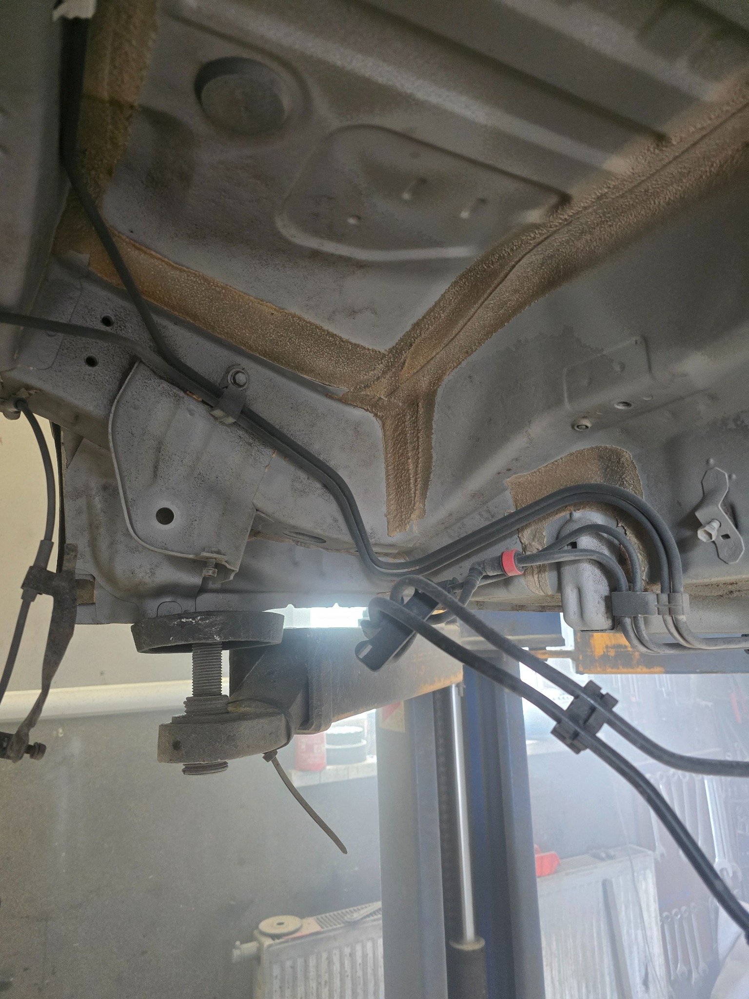 Podwozie samochodu na podnośniku po konserwacji antykorozyjnej. Widoczne przewody, elementy zawieszenia i zabezpieczona powłoka antykorozyjna.