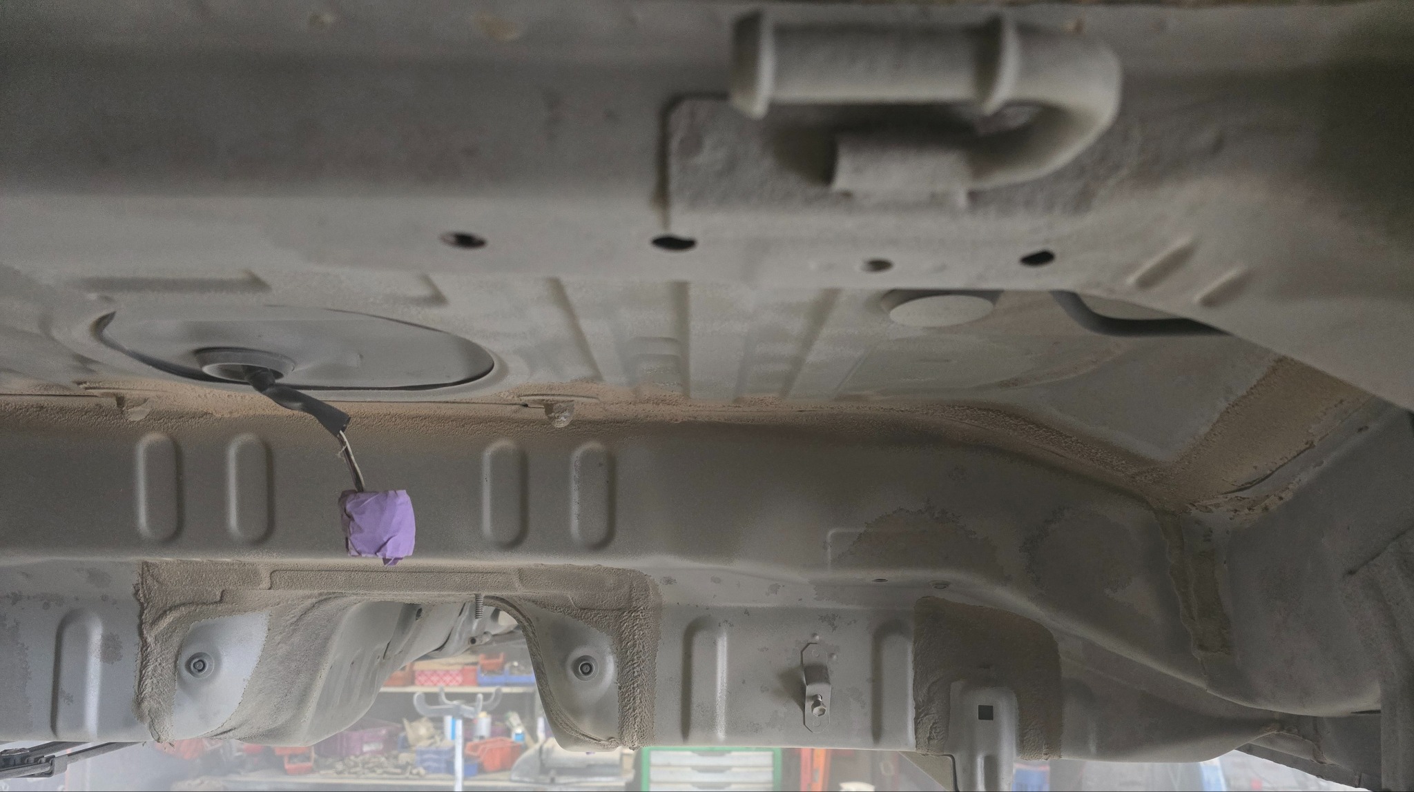Podwozie pojazdu po piaskowaniu i zabezpieczeniu antykorozyjnym, widoczne elementy konstrukcyjne i kabel zabezpieczony fioletową taśmą. Detal z warsztatu.