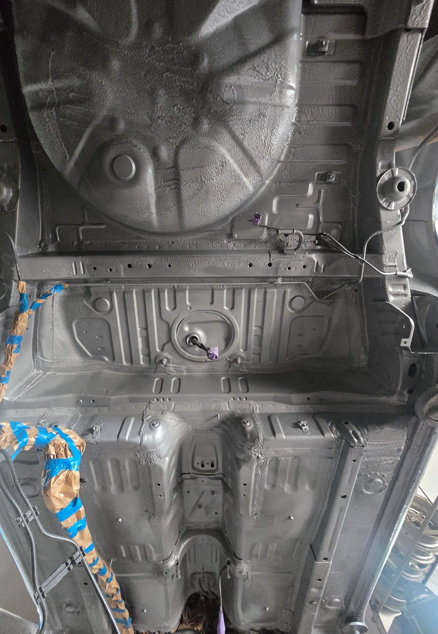 Pomalowane podwozie samochodu na szaro, widok z dołu. Elementy zabezpieczone taśmą malarską. Detal po konserwacji antykorozyjnej.