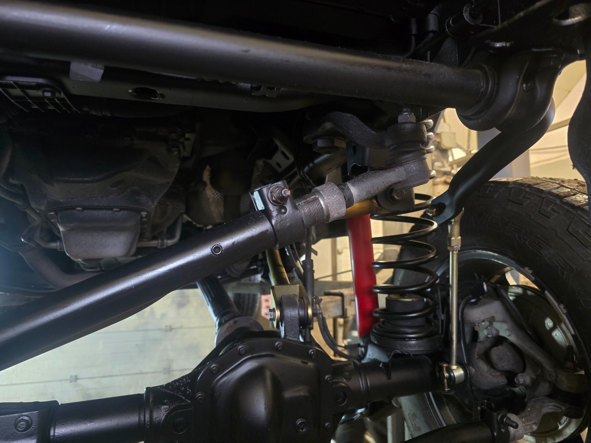 Podwozie samochodu terenowego z widocznym zawieszeniem, amortyzatorem w kolorze czerwonym i elementami układu kierowniczego. Widok od spodu, oświetlenie warsztatowe.