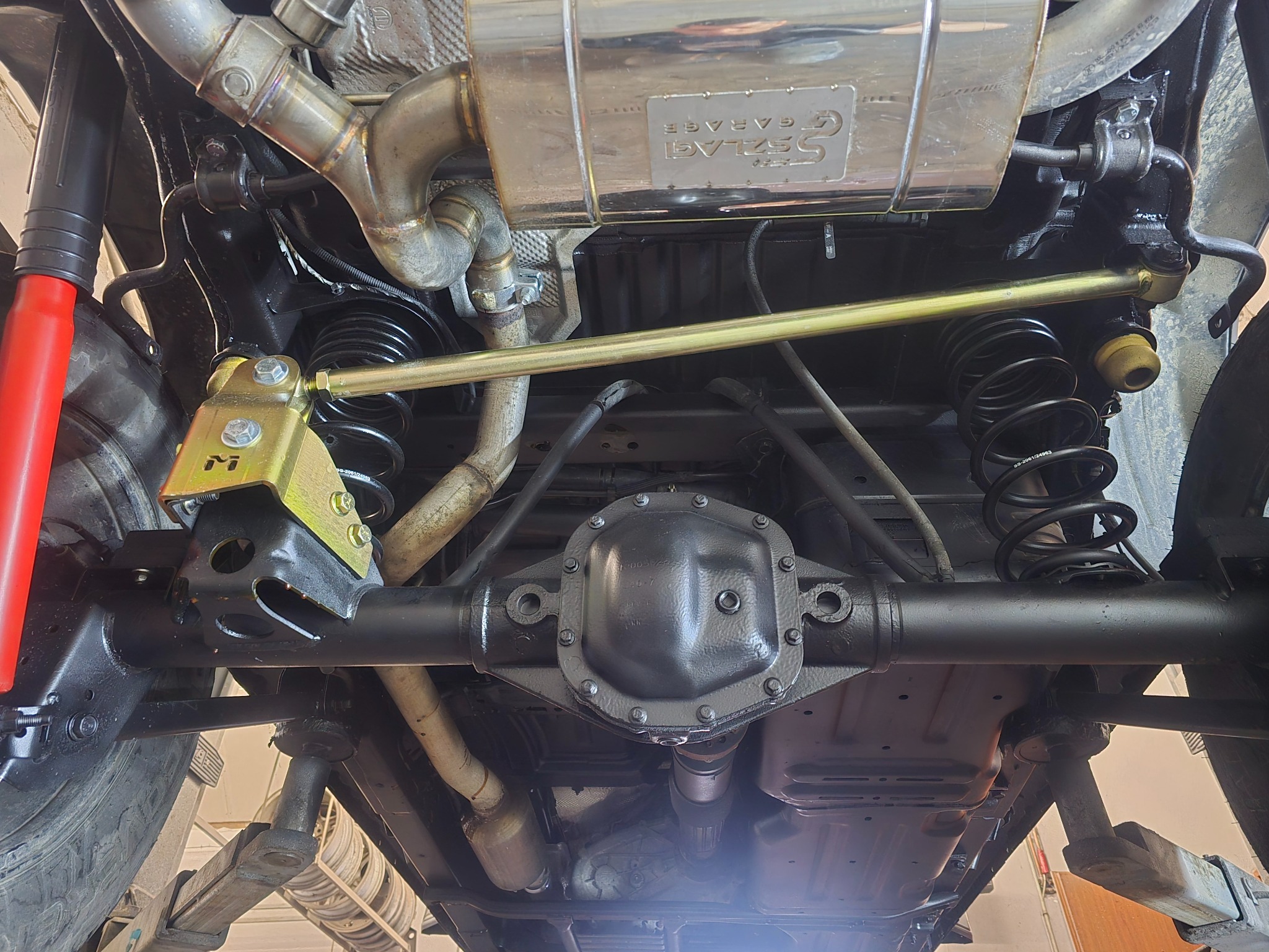 Podwozie samochodu na podnośniku z widocznym układem wydechowym, zawieszeniem i elementami konstrukcyjnymi po konserwacji. Detaliczny widok od dołu.