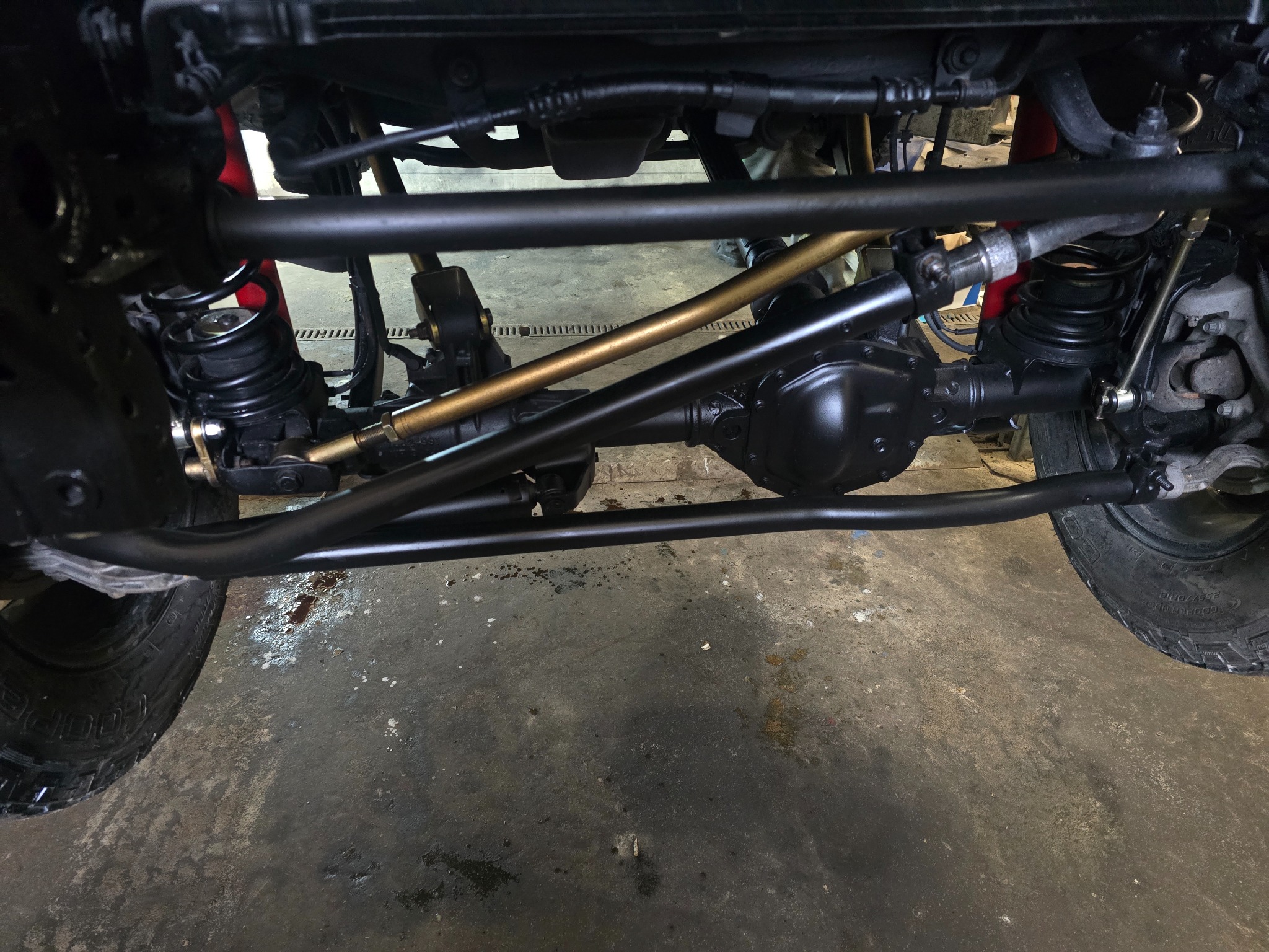Podwozie terenowego auta po konserwacji: czarne elementy zawieszenia, złoty drążek stabilizatora, widoczne sprężyny i opony z agresywnym bieżnikiem.