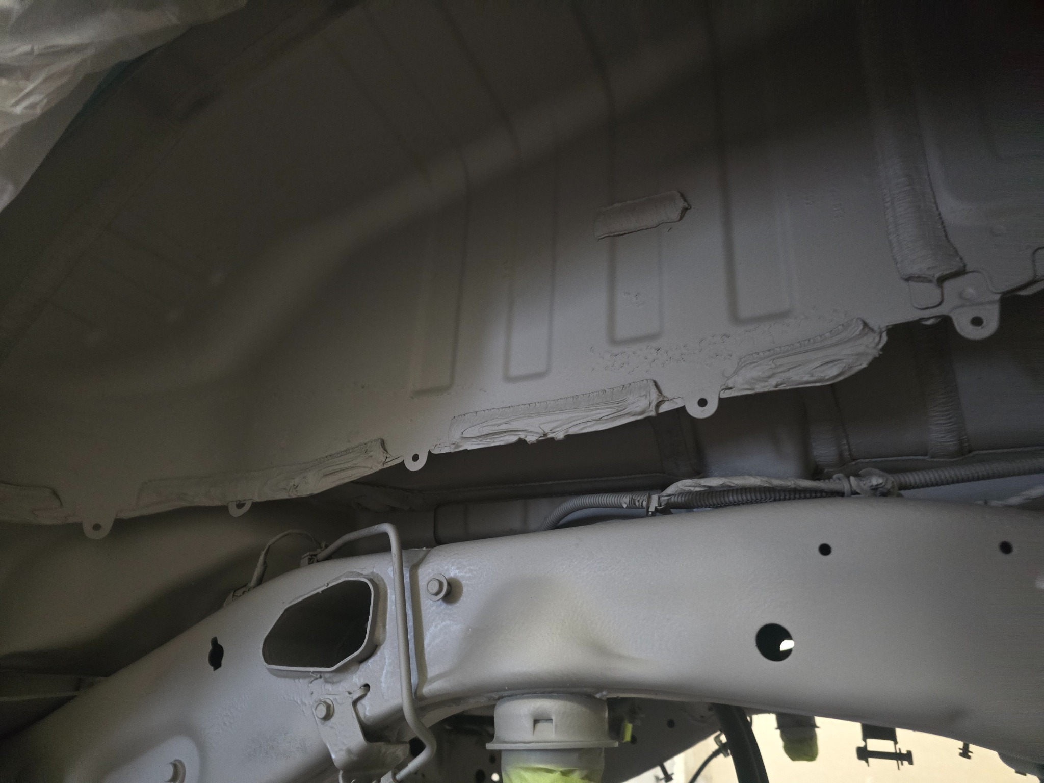 Podwozie samochodu po zabezpieczeniu antykorozyjnym, widoczne elementy ramy i nadwozia pokryte szarą powłoką ochronną. Detale mocowań i przewodów.