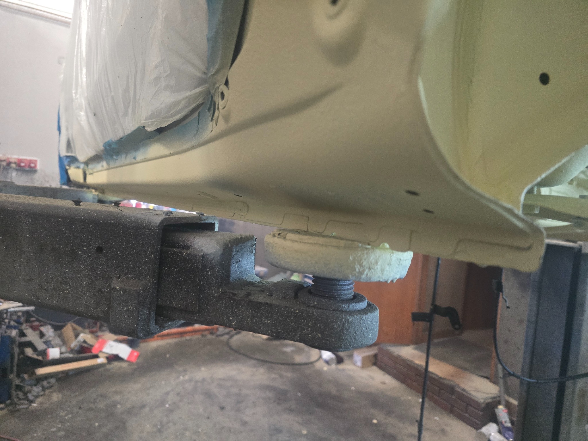 Podwozie auta po konserwacji antykorozyjnej, widoczne na podnośniku warsztatowym, zabezpieczone folią. Jasny lakier, detale podwozia.