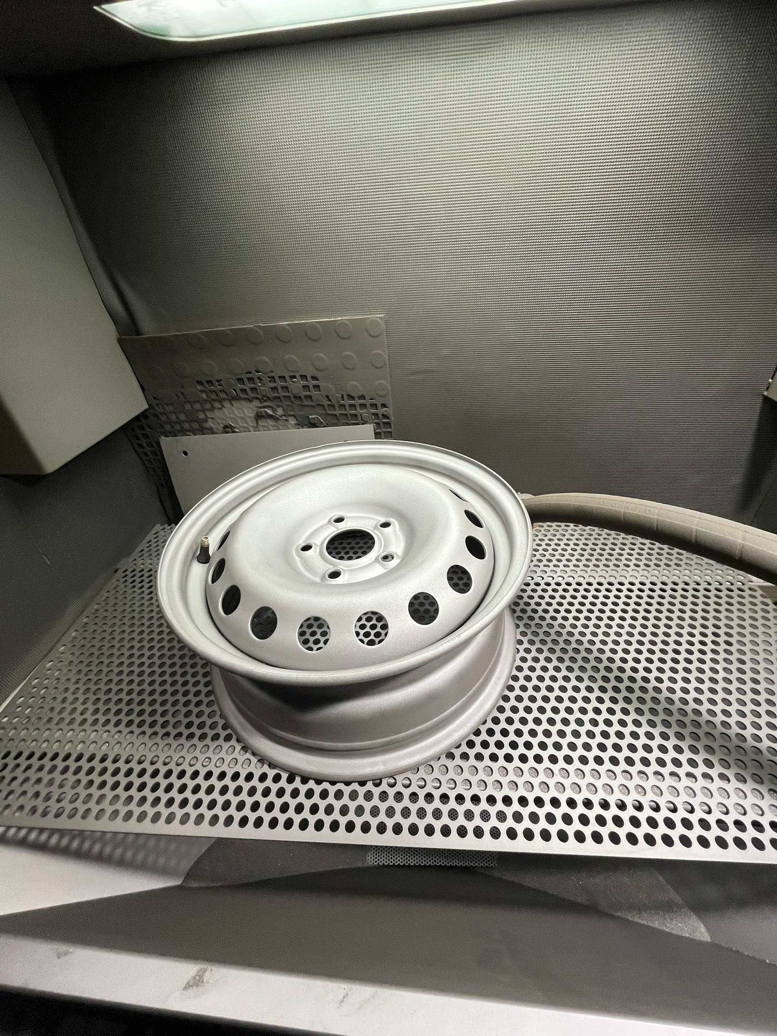 Oczyszczona, pomalowana proszkowo felga samochodowa w komorze do piaskowania, leżąca na perforowanym metalowym ruszcie.