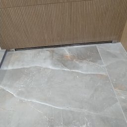 Budownictwo Dawid Prządka - Stylowe wykończenie: szare płytki podłogowe imitujące marmur i panel ścienny z subtelnym, prążkowanym wzorem drewna. Minimalistyczna listwa przypodłogowa.