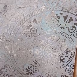 Budownictwo Dawid Prządka - Dekoracyjna ściana w odcieniach szarości z motywem mandali, wykonana techniką szablonową. Widoczne niedoskonałości faktury i subtelne przebarwienia błękitu.