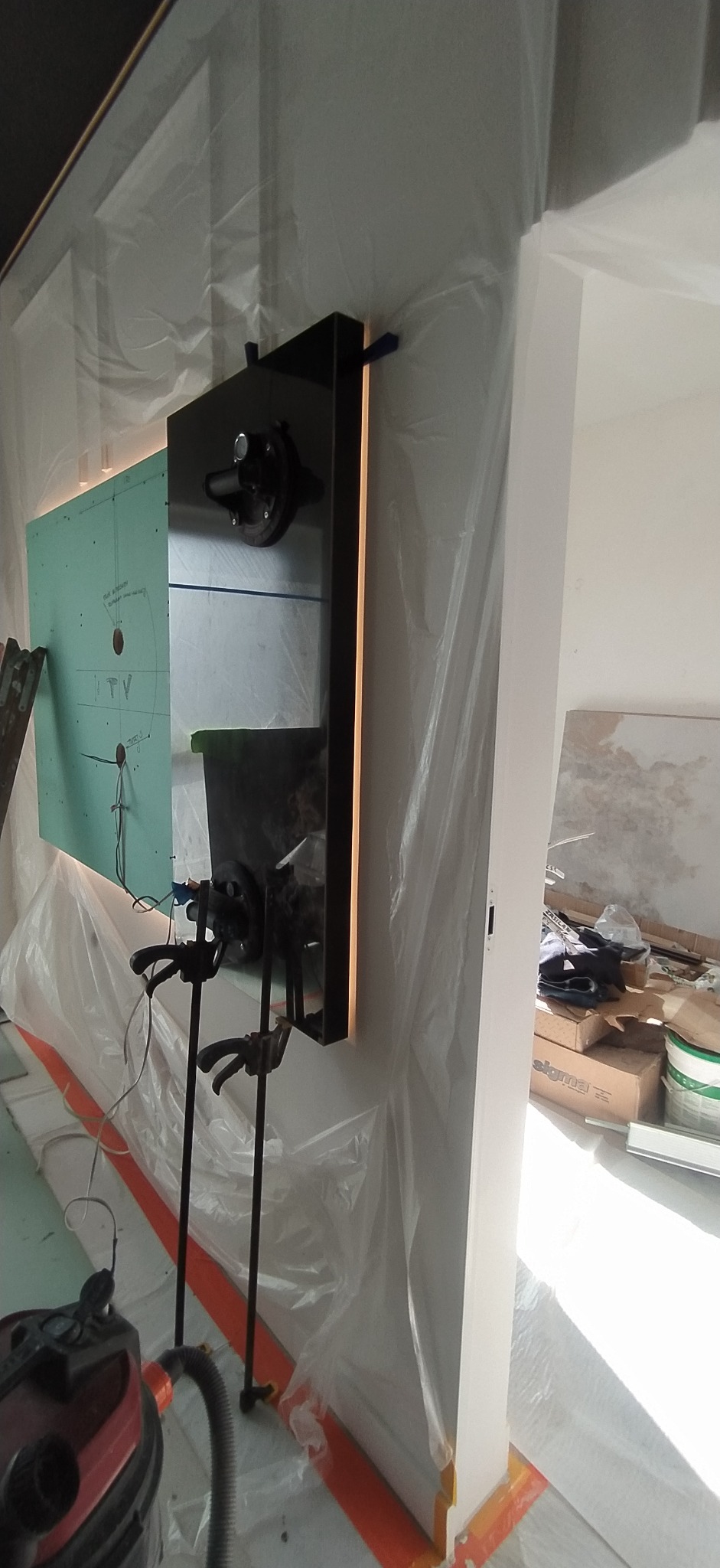 Montaż lustra z podświetleniem LED w Elblągu, zabezpieczone folią malarską. Widoczne narzędzia montażowe i przygotowana ściana z płytą gipsową. Etap prac wykończeniowych.