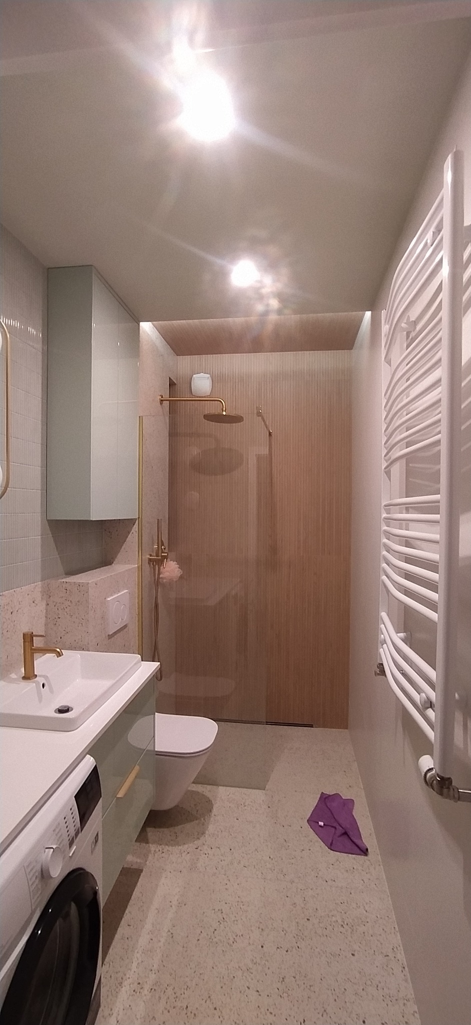 Nowoczesna łazienka z kabiną prysznicową typu walk-in, umywalką na szafce w pastelowym kolorze i grzejnikiem drabinkowym. Wykończenie w jasnych, stonowanych barwach.