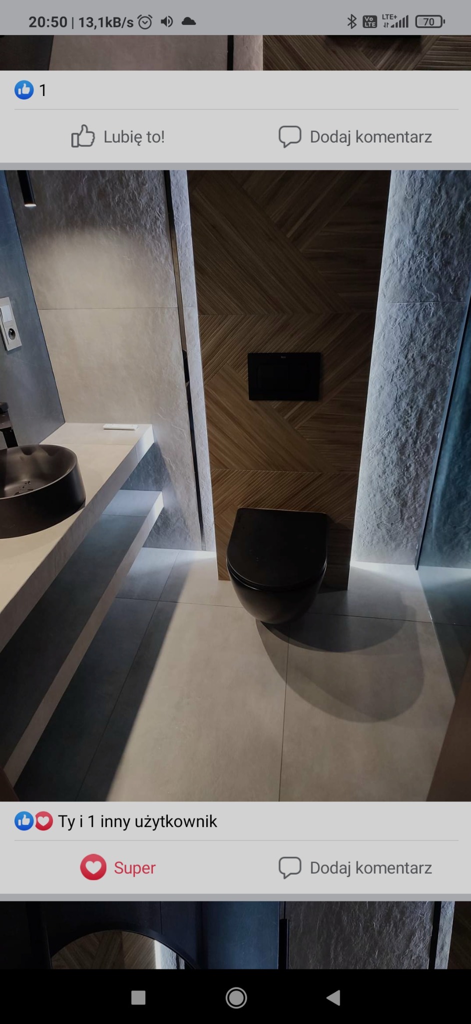 Nowoczesna łazienka z czarną miską WC i umywalką na tle drewnianej ściany z podświetleniem LED. Minimalistyczny design, płytki w odcieniach szarości.