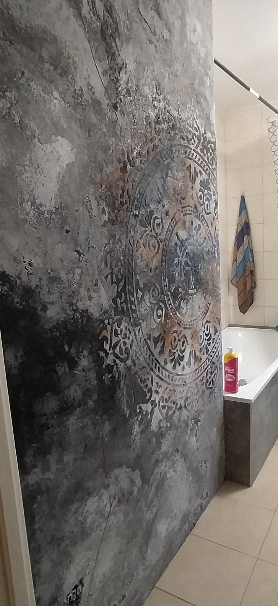 Dekoracyjna ściana w łazience z szarym wzorem mandali, widok na wannę i ręcznik. Wyjątkowa faktura i styl wykończenia.