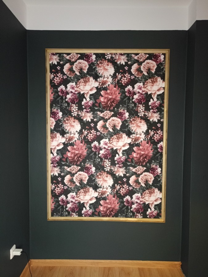 Wzorzysta tapeta w kwiaty w złotej ramie na ciemnozielonej ścianie w pokoju z drewnianą podłogą. Dekoracja wnętrza w klasycznym stylu.