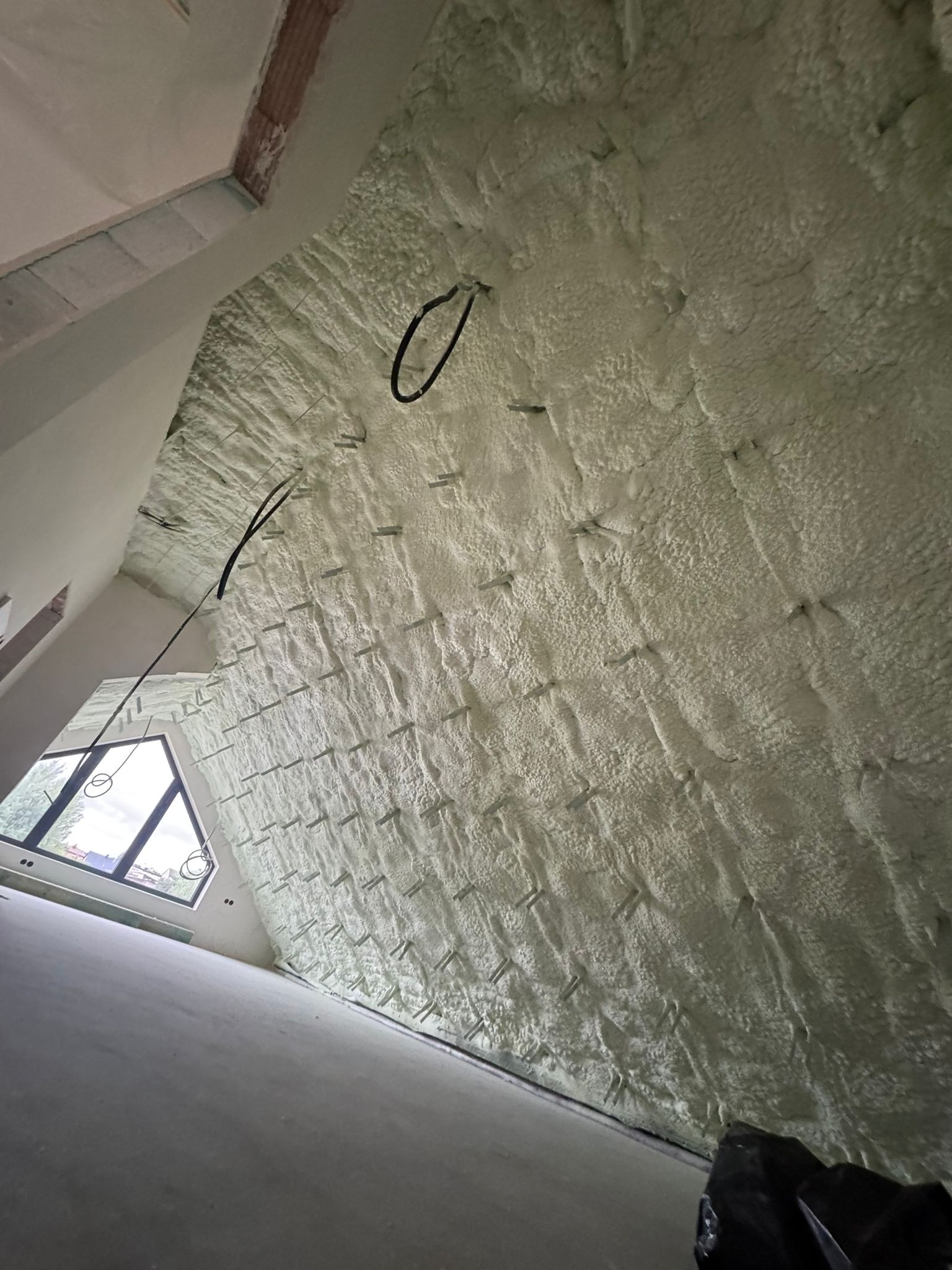 Poddasze po ociepleniu pianką PUR, widoczne szpilki montażowe i przewody elektryczne. Skośna ściana z oknem w tle.