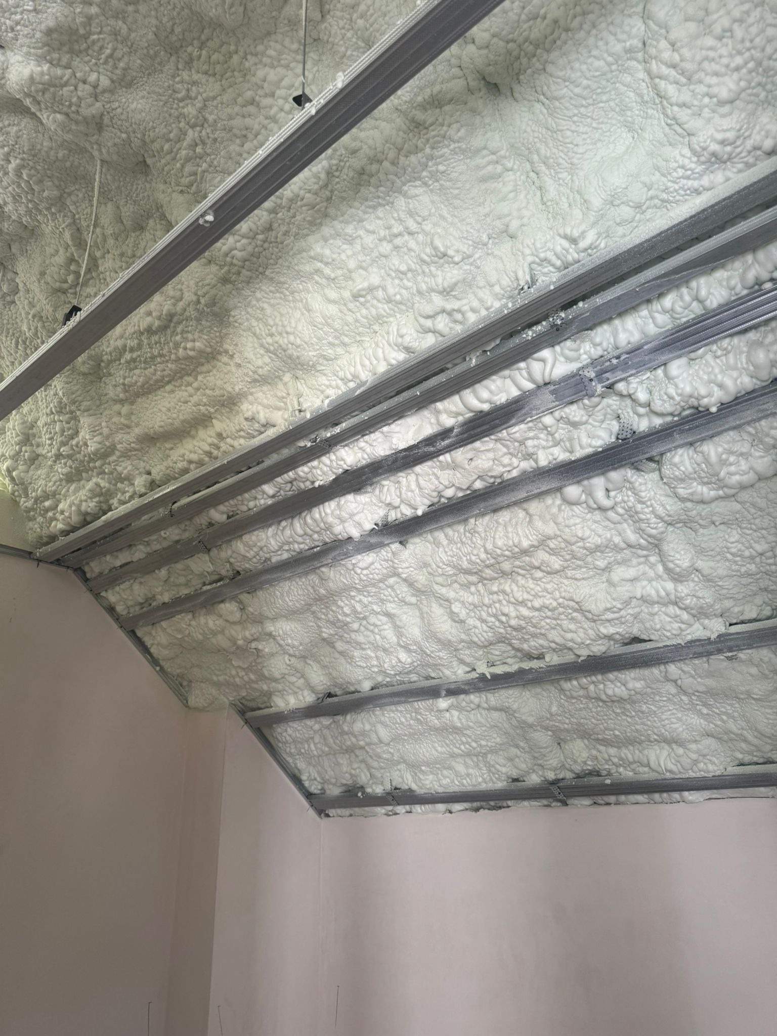 Poddasze ocieplone pianką PUR w Jędrzejowie. Widoczne metalowe profile konstrukcyjne i nałożona, nierównomierna warstwa izolacji. Ocieplanie natryskowe.