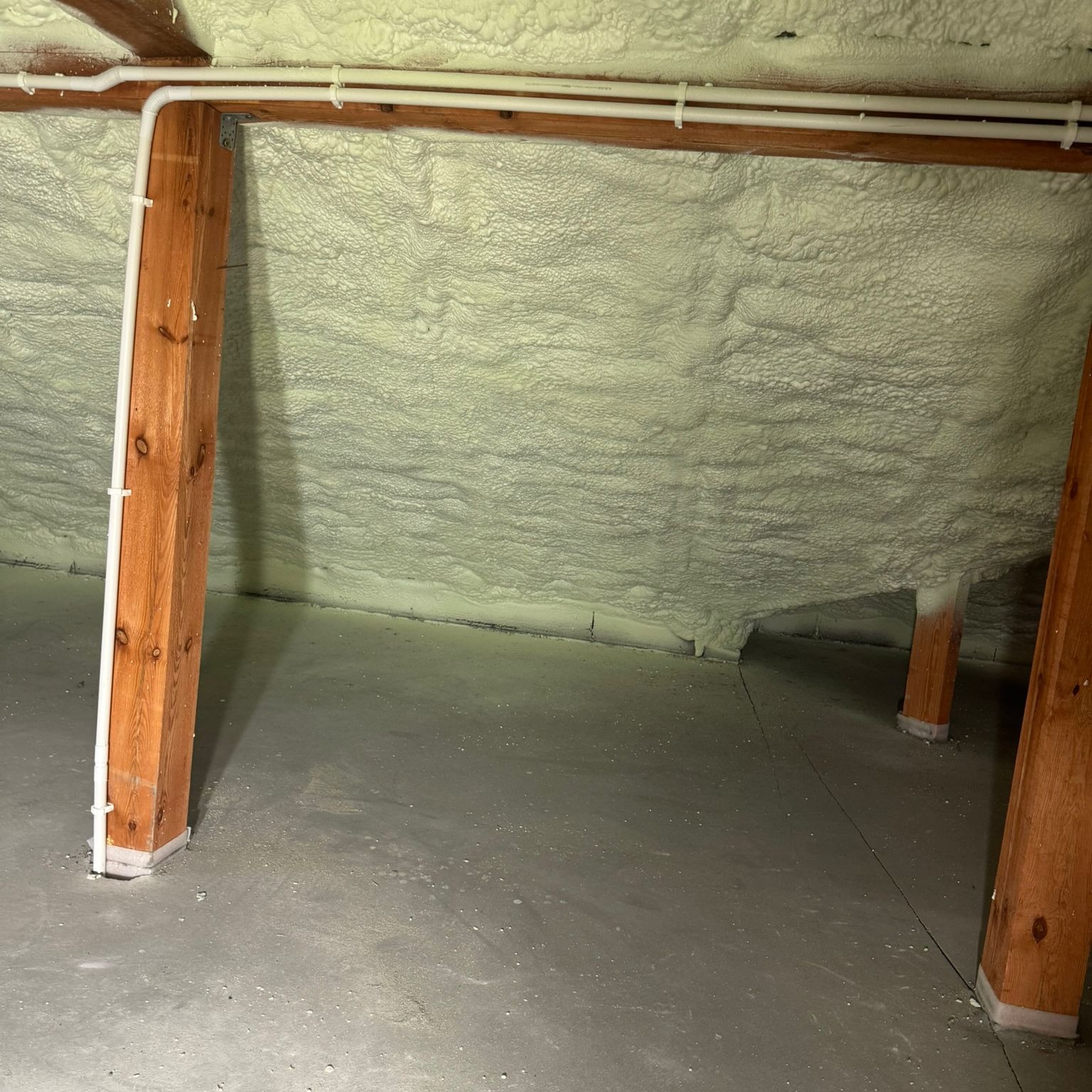 Poddasze po ociepleniu pianką PUR, widoczne drewniane belki i białe rury. Izolacja pokrywa skosy dachu tworząc jednolitą, porowatą strukturę.