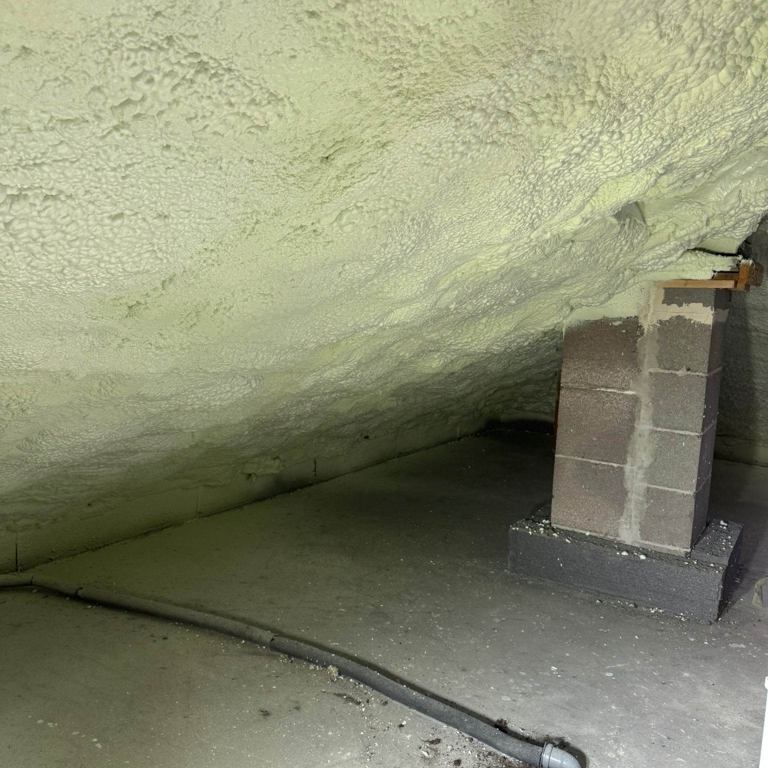 Poddasze po ociepleniu pianką PUR, widoczny komin z cegły i przewody. Izolacja pokrywa skośny sufit, tworząc jednolitą warstwę. Kąt ujęcia z dołu.