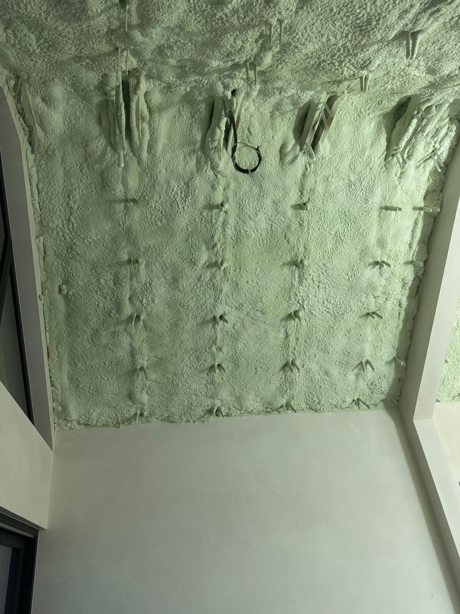 Poddasze ocieplone pianką PUR z widocznymi elementami mocującymi, świeżo po aplikacji, struktura pianki dobrze widoczna, jasne oświetlenie.