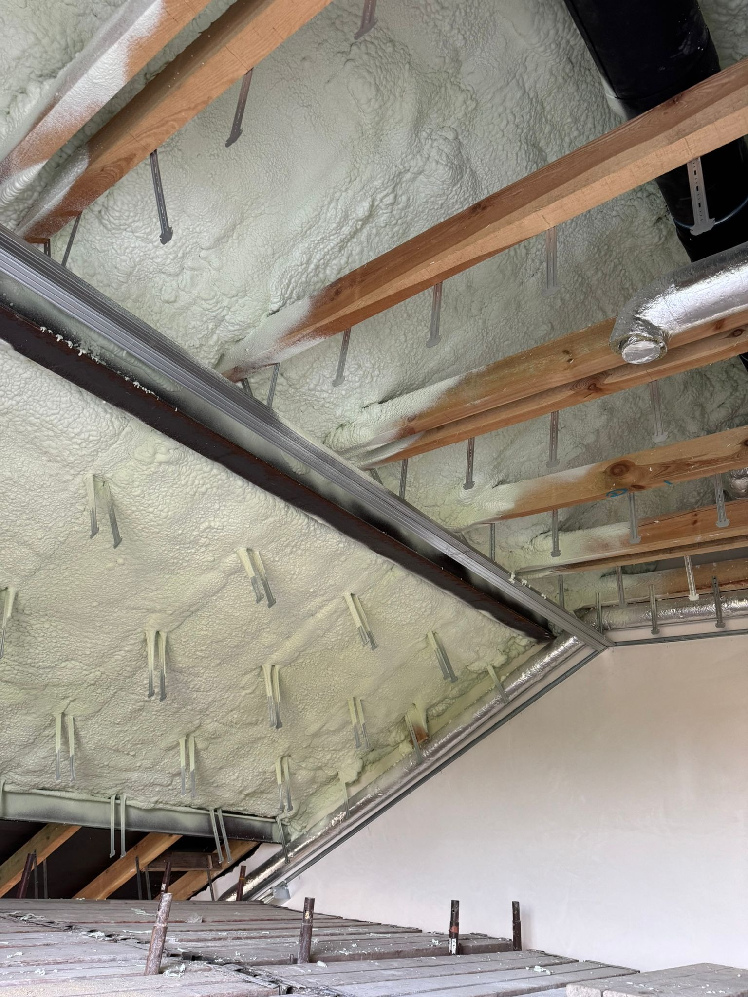 Poddasze ocieplone pianką PUR z widocznymi elementami konstrukcji drewnianej i metalowej. Aplikacja pianki równomierna, pokrywająca całą powierzchnię.