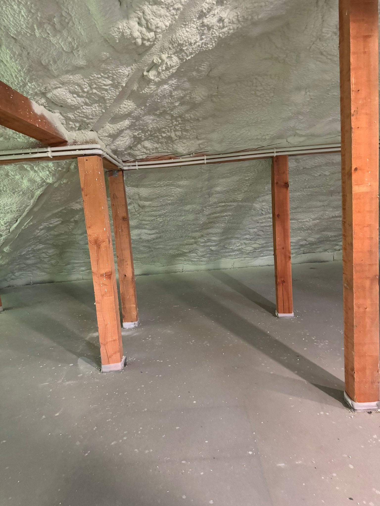 Poddasze po ociepleniu pianką PUR: drewniane słupy, biała pianka na skośnym dachu, widoczne rury instalacyjne.