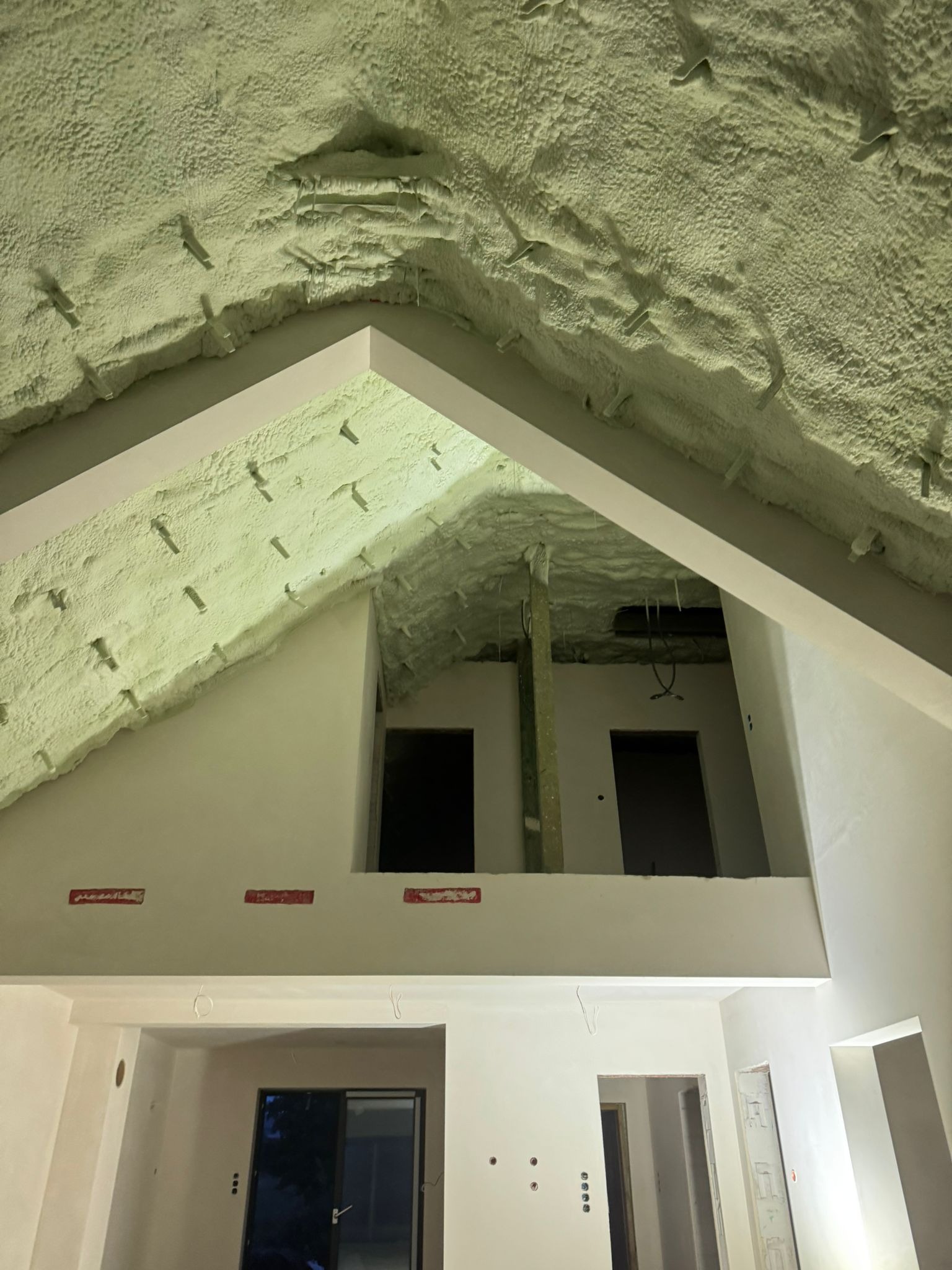 Poddasze po ociepleniu pianką PUR, widoczne krokwie i konstrukcja dachu pokryte warstwą izolacji. Surowy stan wnętrza, przygotowany do dalszych prac wykończeniowych.