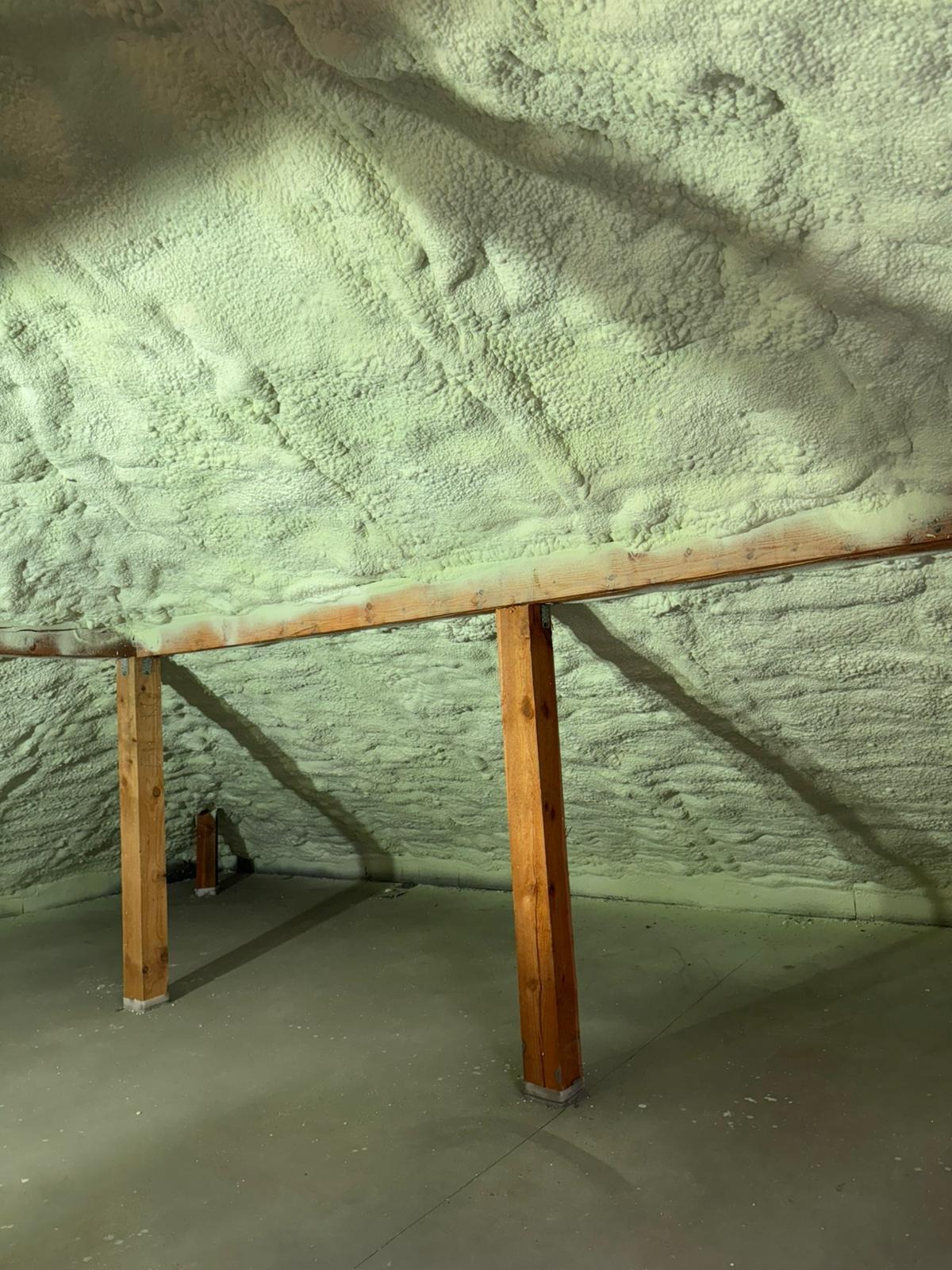 Poddasze po ociepleniu pianką PUR, widoczne drewniane belki konstrukcyjne i nierównomierna powierzchnia izolacji w odcieniach bieli i beżu.