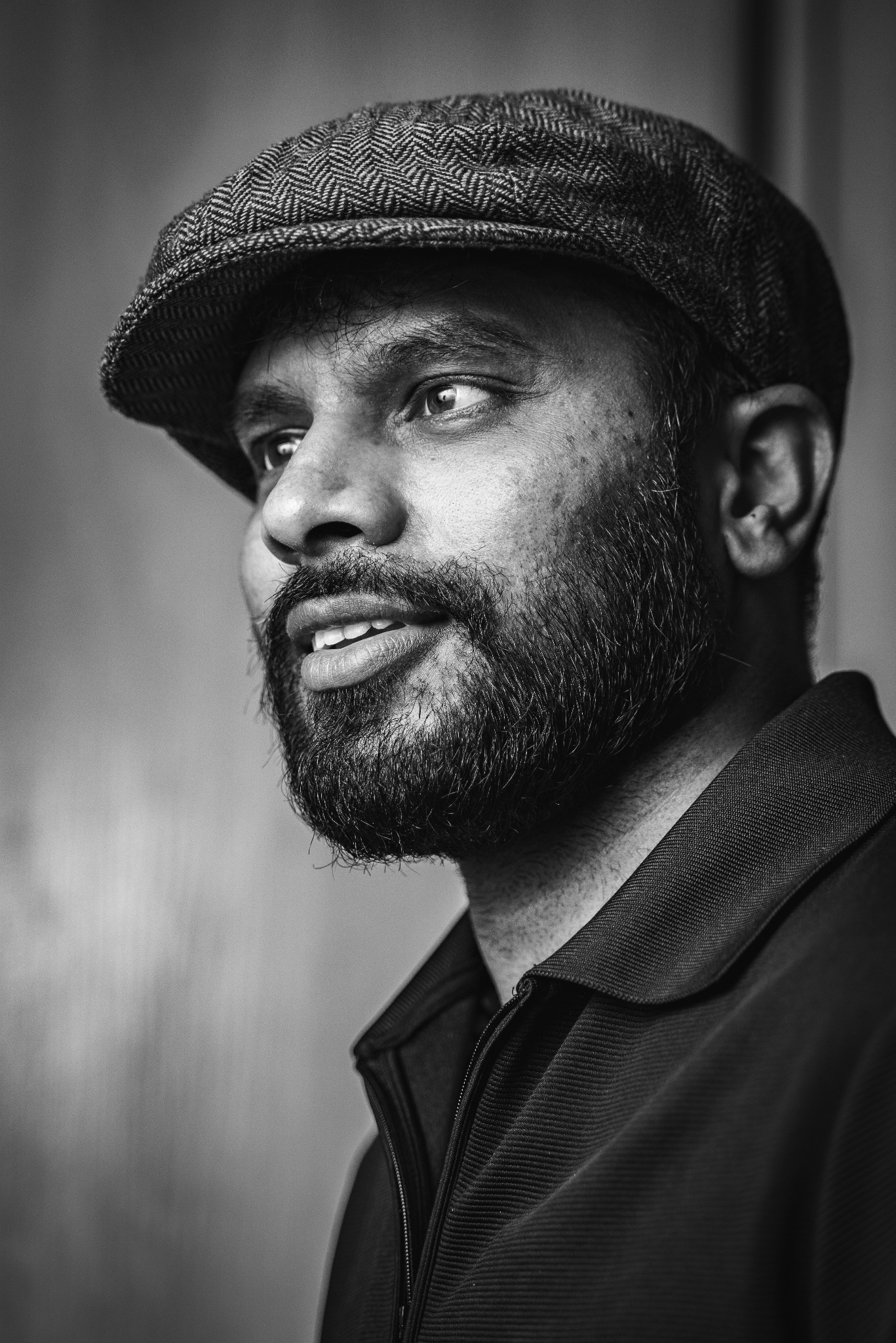 Portret mężczyzny z brodą i kaszkietem w czerni i bieli, spoglądającego w lewo.