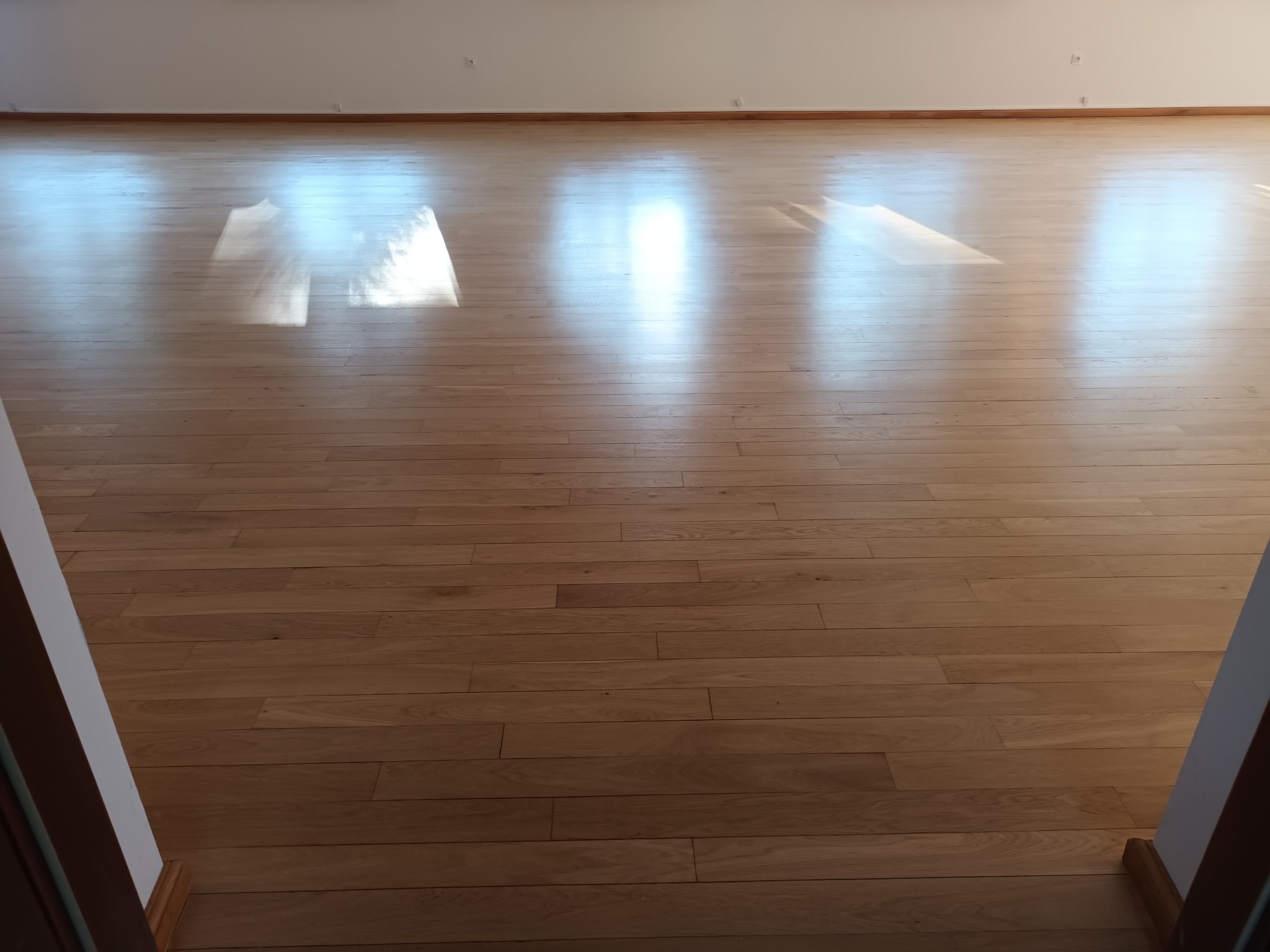 Jasna, drewniana podłoga z parkietu, oświetlona wpadającym światłem słonecznym, widok z perspektywy wejścia do pomieszczenia.