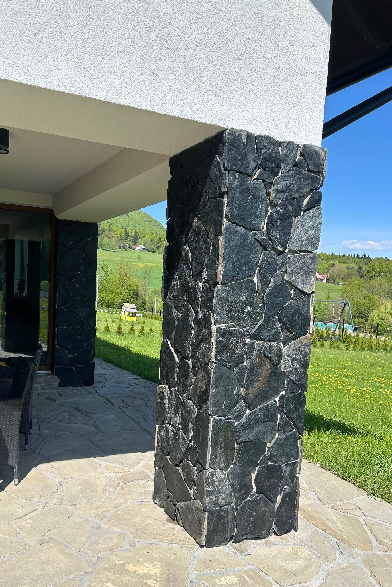 Kamienna okładzina filaru domu w Gorlicach, z widokiem na zielony krajobraz. Naturalne materiały wykończeniowe i precyzyjne wykonanie.