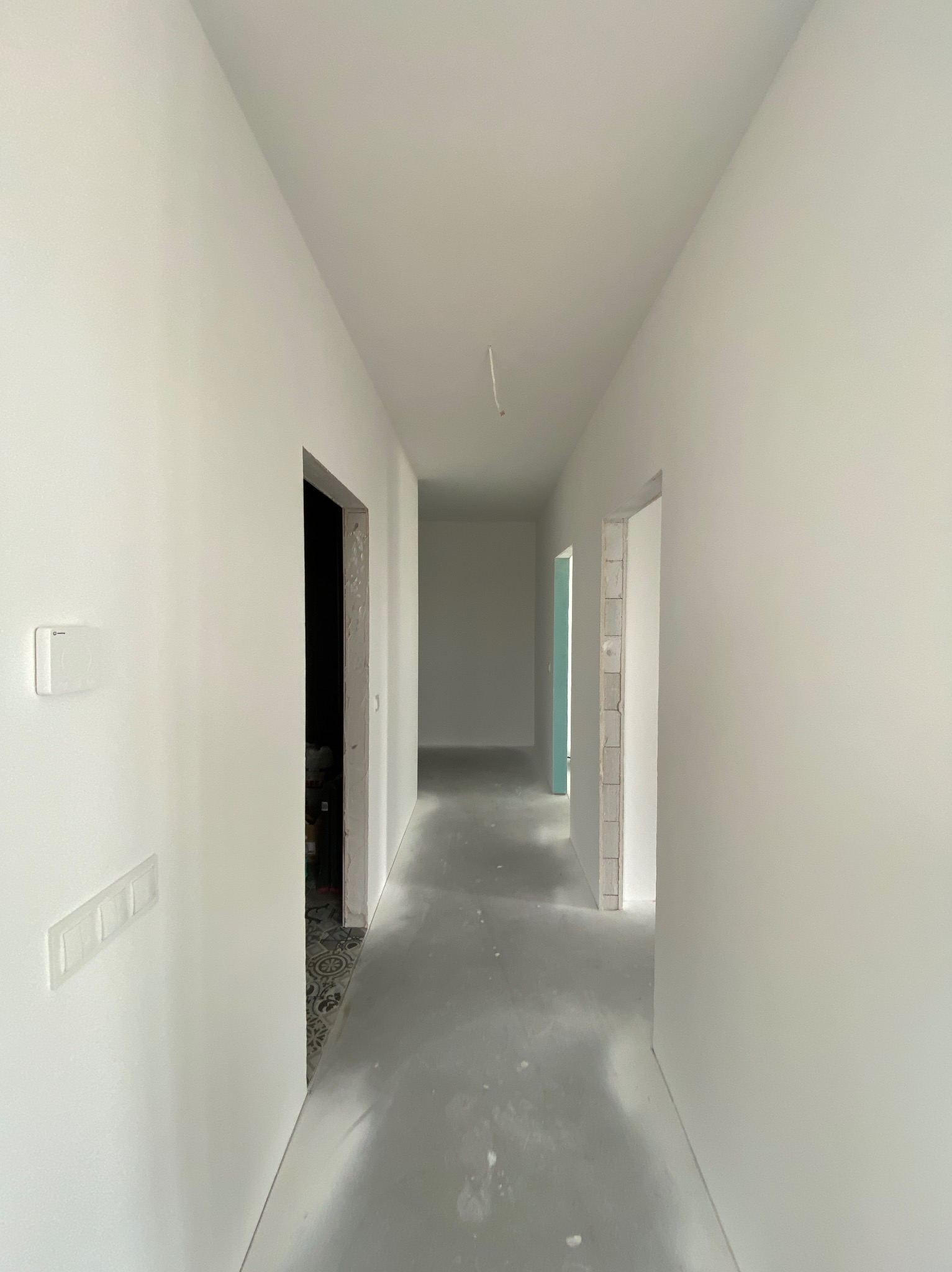 Biały korytarz w trakcie remontu, widoczne surowe ściany po szpachlowaniu i wylewka podłogowa, przygotowanie do malowania i wykończenia.